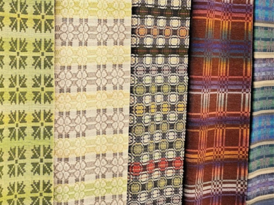 Vertikāli izvietoti pieci austu audumu paraugi ar atšķirīgiem rakstiem: gaiši zaļš ar stilizētām zvaigznēm, bēšs ar smalkiem savienotiem aplīšiem, tumšs ar krāsainiem ģeometriskiem astoņstūriem, brūns rūtains un zili-zaļš svītrains.